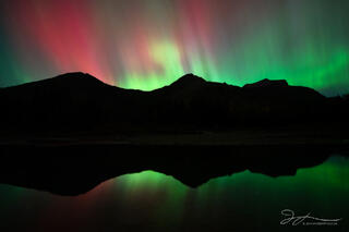 Green and pink aurora dance in the sky above mountains.
