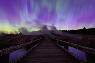 A bridge in Yellowstone with a sky full of aurora.