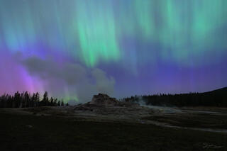 A colorful sky full of aurora dances above Castle Geyser in Yellowstone.