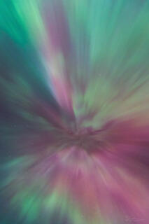 A pink and green coronal aurora radiates in the sky above Yellowstone.