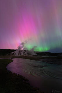 A pink and green aurora is reflected in the Firehole River.