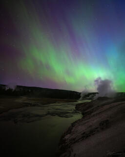 An aurora dances above the Firehole River and thermal features in Yellowstone.