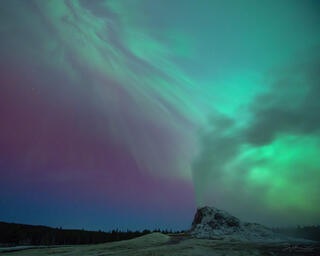 White dome geyser erupting under an aurora in Yellowstone.
