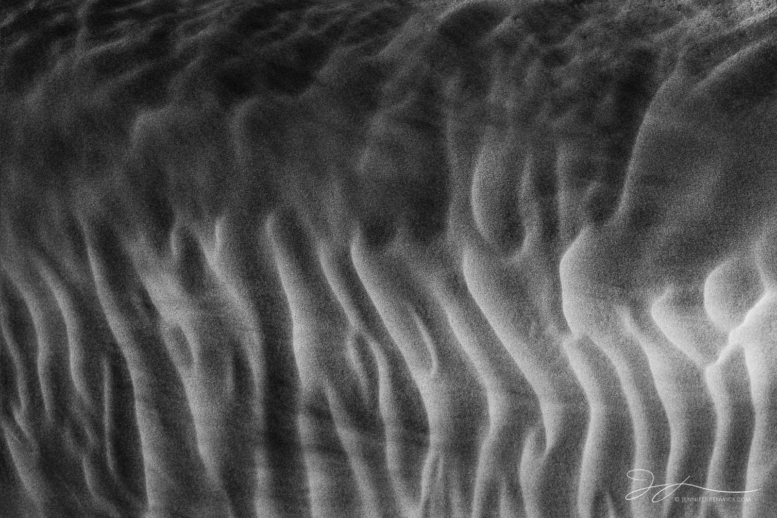 The wind sweeps sand grains across flame-like patterns on the side of a sand dune during a windstorm.