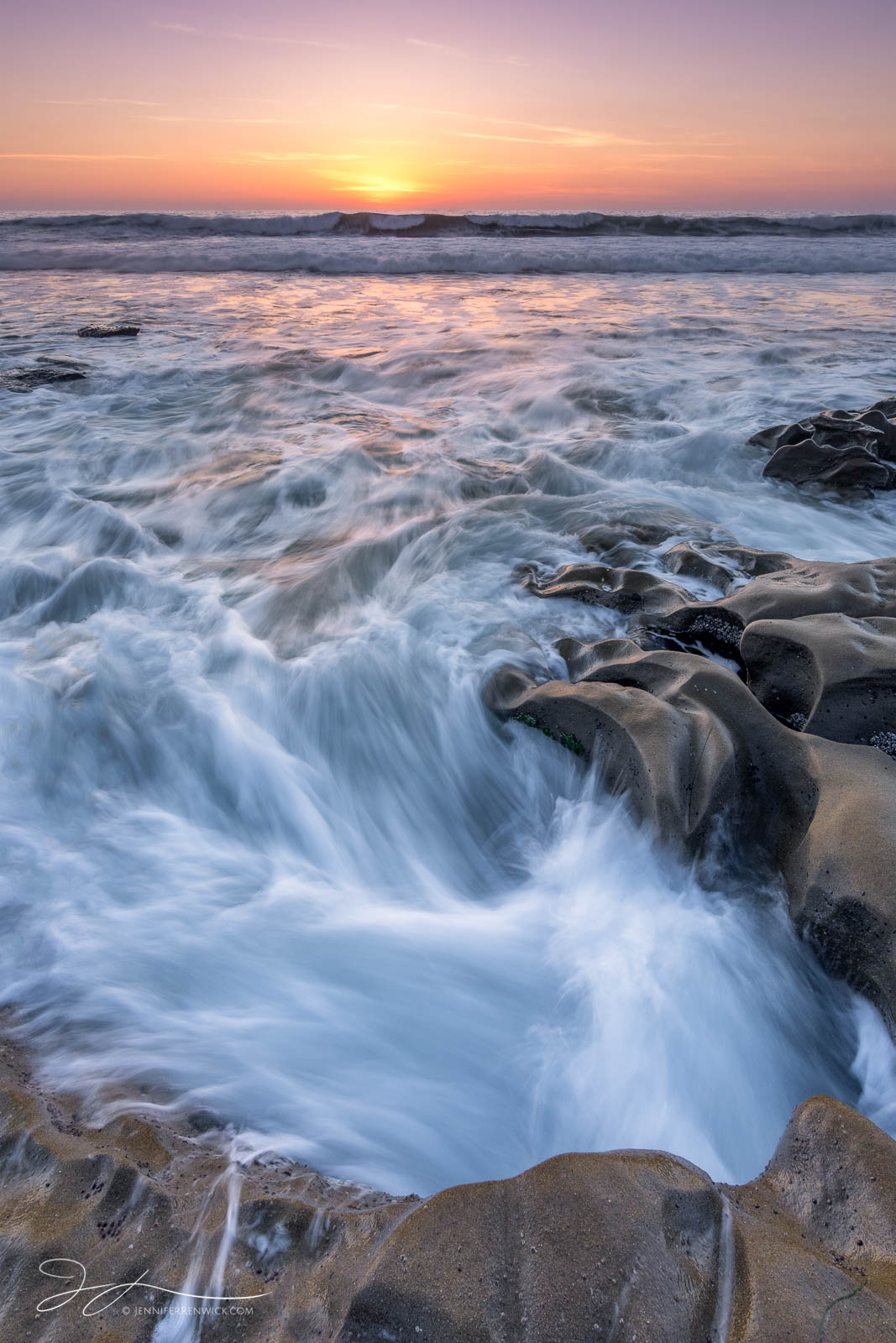 The sun sets over a rocky beach in La Jolla, California.