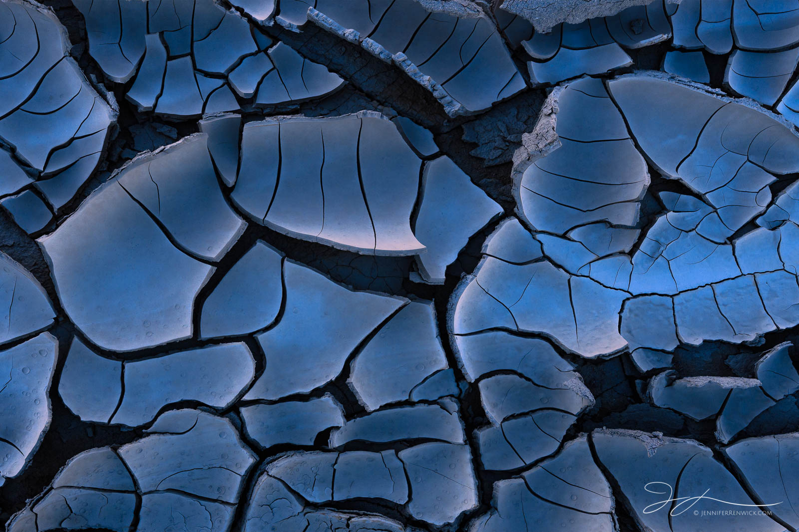 Morning light during the blue hour reflects off mud crack tiles on a playa, creating a blue glow.