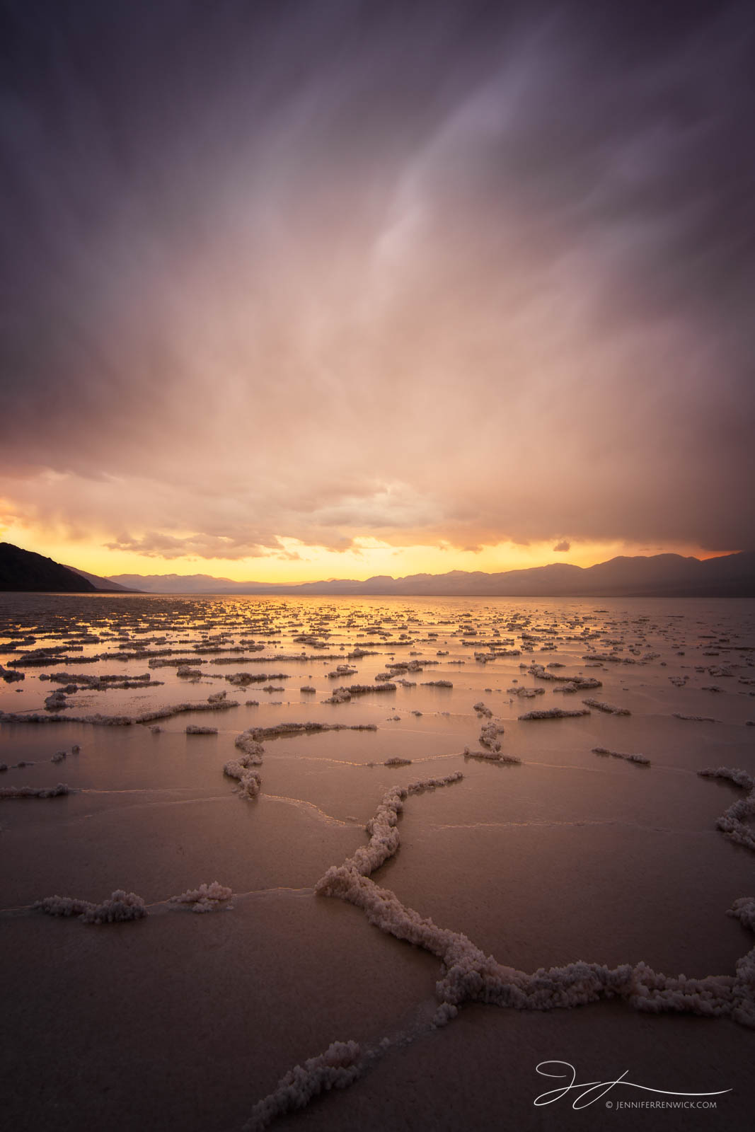 Dissolving salt polygons on Badwater Basin sit under glowing stormy skies during a beautiful sunset.