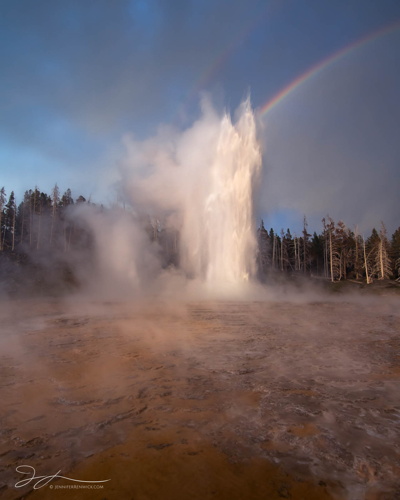 Grand Geyser erupts under stormy skies and a double rainbow.