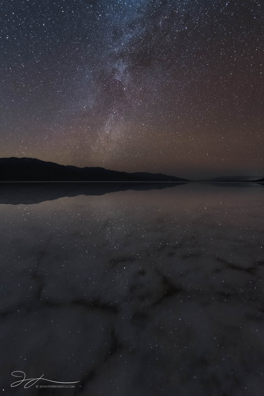 The night sky, complete with a meteor and winter milky way reflects onto a flooded Badwater Basin in Death Valley National park...